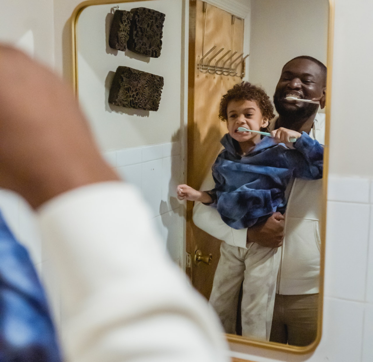 A father and son brush their teeth as they look in the mirror